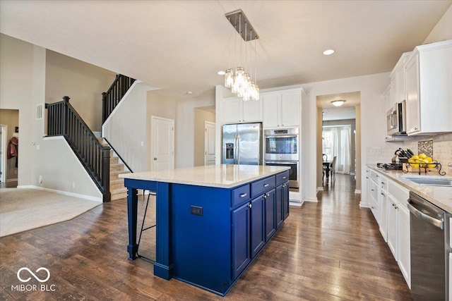 kitchen with appliances with stainless steel finishes, a kitchen island, pendant lighting, blue cabinets, and white cabinetry