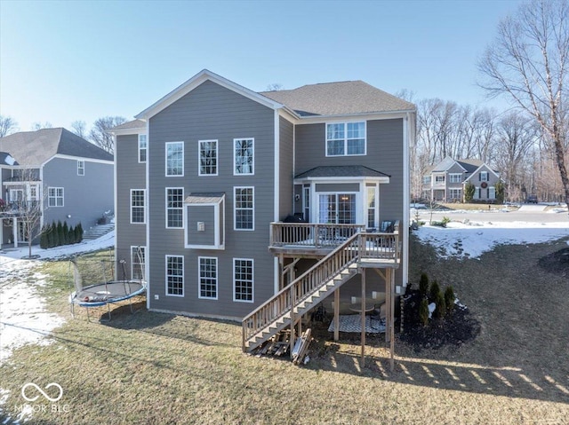 back of property featuring a trampoline, a wooden deck, and a lawn