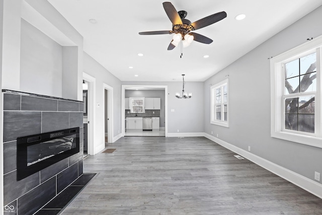 unfurnished living room with ceiling fan with notable chandelier, a fireplace, and hardwood / wood-style flooring