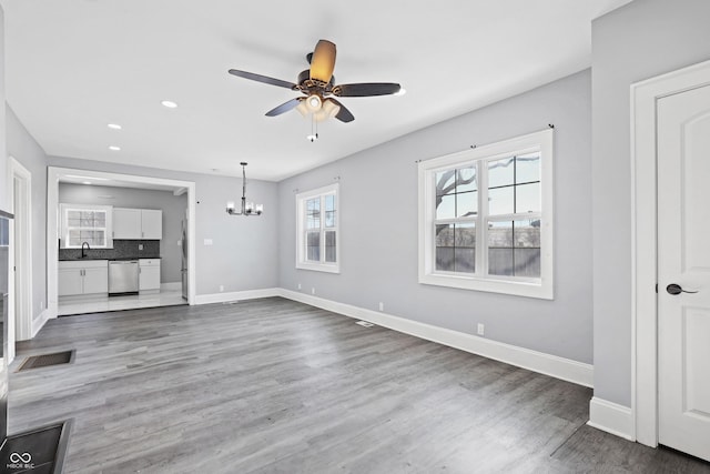 unfurnished living room with wood-type flooring, sink, and ceiling fan with notable chandelier