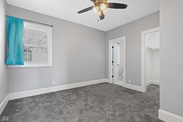 unfurnished bedroom featuring ceiling fan, dark colored carpet, ensuite bath, a closet, and a walk in closet