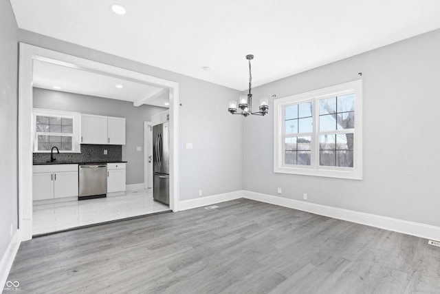 unfurnished dining area with beamed ceiling, sink, a chandelier, and light hardwood / wood-style floors