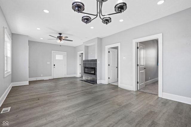 unfurnished living room featuring ceiling fan with notable chandelier, dark hardwood / wood-style floors, and a tiled fireplace