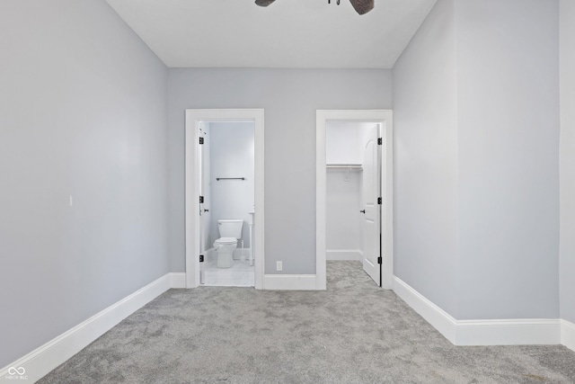 unfurnished bedroom with a spacious closet, light carpet, ensuite bathroom, ceiling fan, and a closet