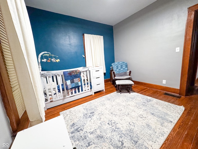 bedroom with wood-type flooring and a nursery area