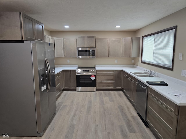 kitchen with light wood-type flooring, stainless steel appliances, a textured ceiling, and sink