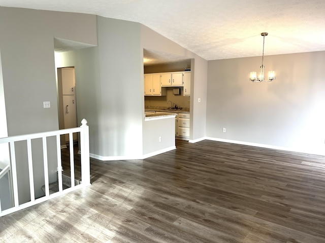 unfurnished living room featuring lofted ceiling, sink, an inviting chandelier, a textured ceiling, and dark hardwood / wood-style flooring