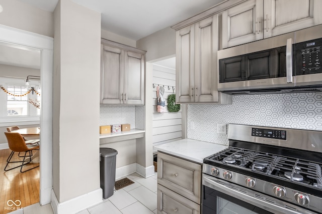 kitchen with light tile patterned floors, light stone counters, baseboards, appliances with stainless steel finishes, and decorative backsplash