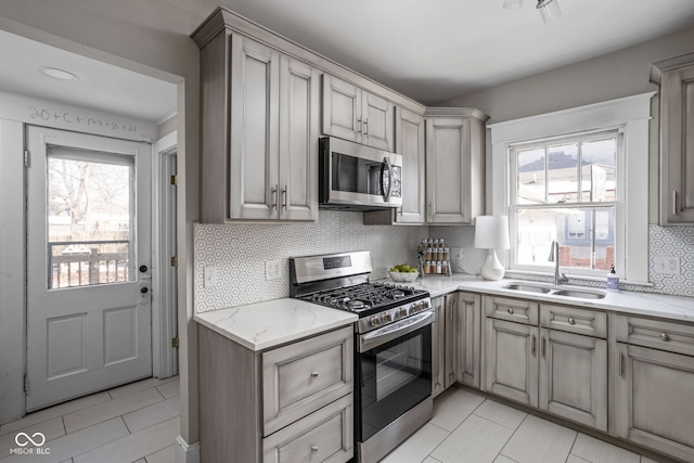 kitchen featuring appliances with stainless steel finishes, a sink, light stone counters, and tasteful backsplash