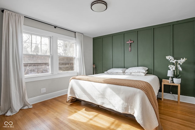 bedroom featuring a decorative wall, light wood-style flooring, and baseboards