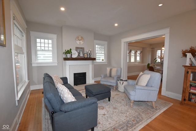 living room with baseboards, recessed lighting, a fireplace with flush hearth, and light wood-style floors