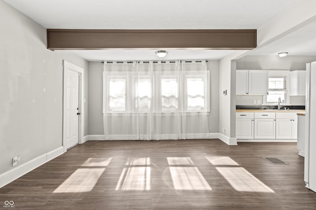 unfurnished living room featuring dark hardwood / wood-style floors, beam ceiling, and sink