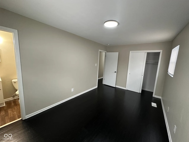 unfurnished bedroom with a closet, connected bathroom, and dark hardwood / wood-style floors