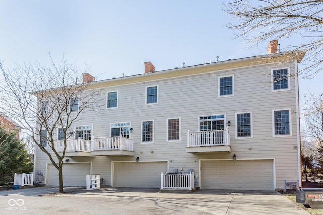 rear view of house featuring a garage, a chimney, and central AC