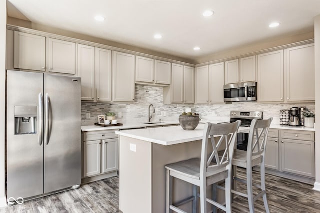 kitchen featuring a kitchen island, light countertops, appliances with stainless steel finishes, dark wood-style floors, and a sink