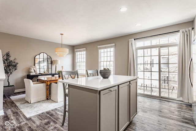 kitchen with dark wood-type flooring, gray cabinetry, a kitchen breakfast bar, a kitchen island, and light countertops