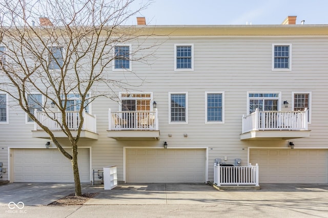 back of house featuring central AC unit, an attached garage, a chimney, and driveway