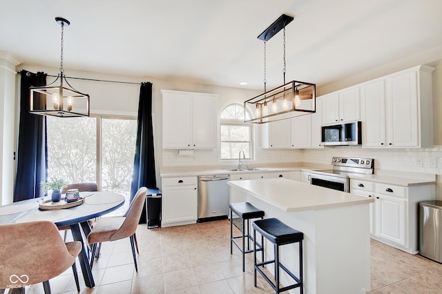 kitchen with appliances with stainless steel finishes, white cabinets, a kitchen island, sink, and pendant lighting