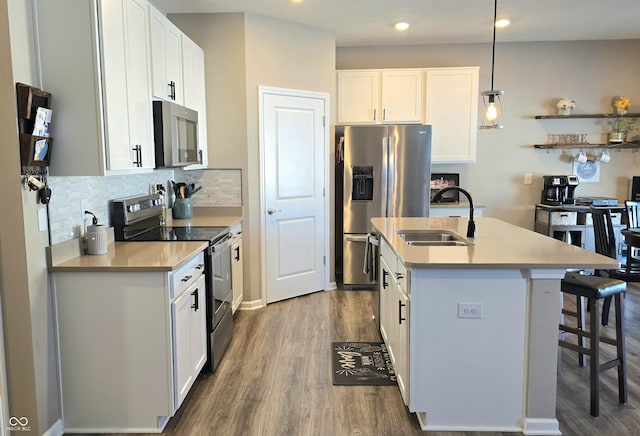 kitchen featuring white cabinets, decorative light fixtures, stainless steel appliances, sink, and a kitchen island with sink