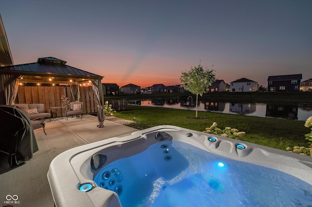 pool at dusk with a water view, a gazebo, a hot tub, and a yard