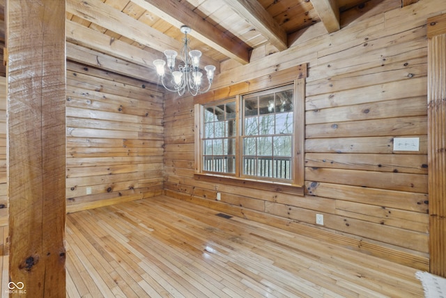 empty room with hardwood / wood-style flooring, wooden walls, wooden ceiling, a chandelier, and beamed ceiling