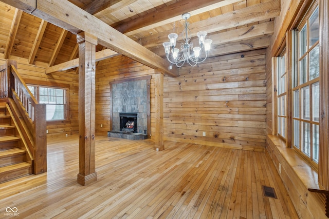 unfurnished dining area with wood walls, wooden ceiling, light hardwood / wood-style flooring, a tile fireplace, and beamed ceiling