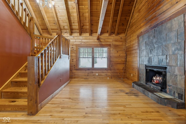 unfurnished living room with wood ceiling, wooden walls, light hardwood / wood-style floors, beam ceiling, and a tiled fireplace