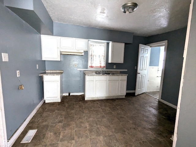 kitchen with a textured ceiling, white cabinets, and sink