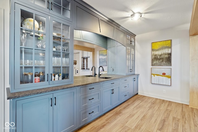 bar with light wood-style flooring, a textured ceiling, baseboards, and a sink