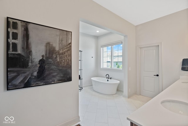 full bath featuring double vanity, a freestanding bath, a sink, tile patterned flooring, and baseboards