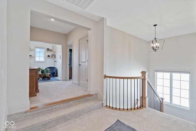 hallway with a chandelier, light carpet, an upstairs landing, visible vents, and baseboards