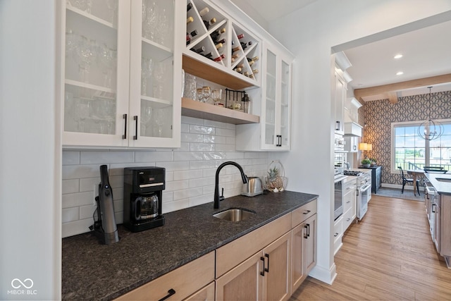 kitchen with light brown cabinets, dark stone countertops, a sink, and glass insert cabinets