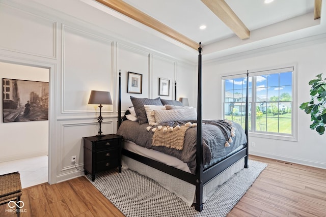 bedroom featuring light wood finished floors, baseboards, and beam ceiling