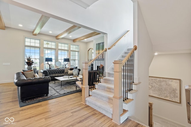 living room featuring baseboards, beamed ceiling, light wood finished floors, and stairs