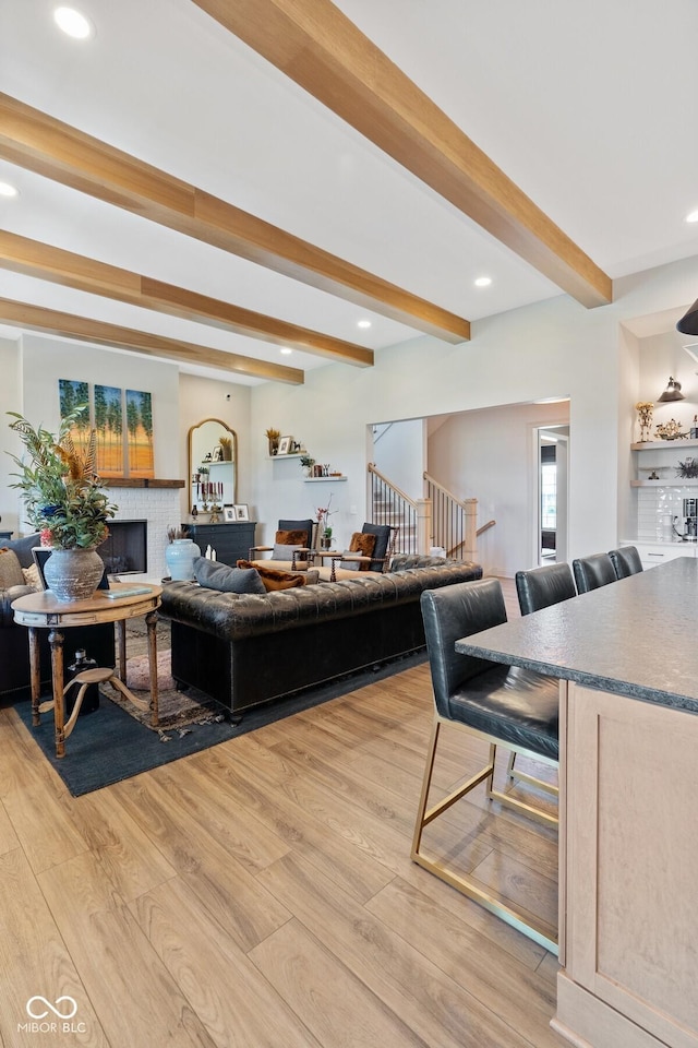 living room featuring light wood finished floors, stairway, beamed ceiling, a fireplace, and recessed lighting