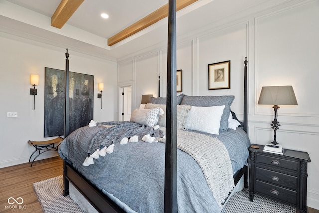 bedroom with recessed lighting, a decorative wall, wood finished floors, beamed ceiling, and baseboards