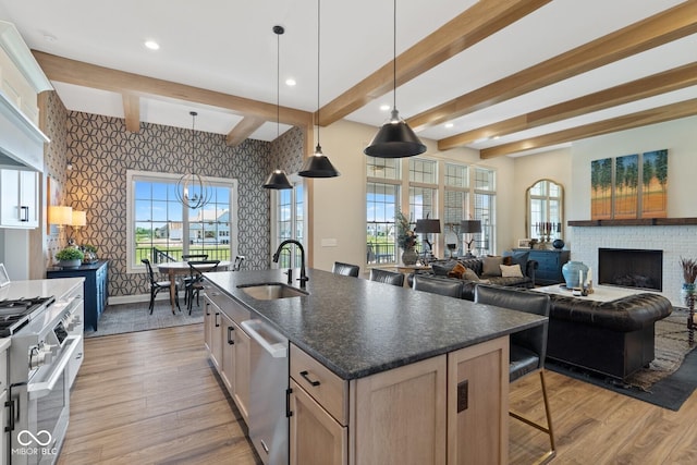 kitchen with wallpapered walls, an island with sink, appliances with stainless steel finishes, open floor plan, and decorative light fixtures