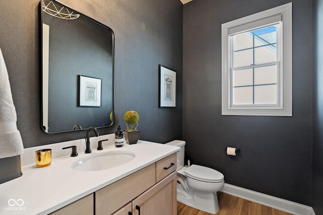 half bathroom with baseboards, vanity, toilet, and wood finished floors