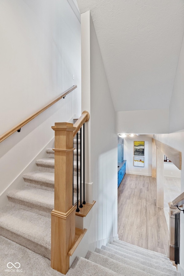 stairway featuring lofted ceiling, a textured ceiling, baseboards, and wood finished floors