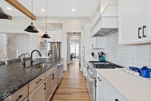 kitchen featuring white cabinets, premium appliances, custom range hood, decorative light fixtures, and a sink