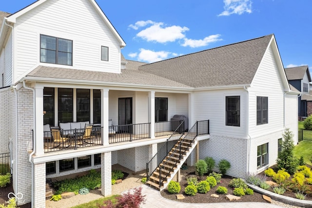 view of front of home featuring covered porch, brick siding, stairway, and roof with shingles