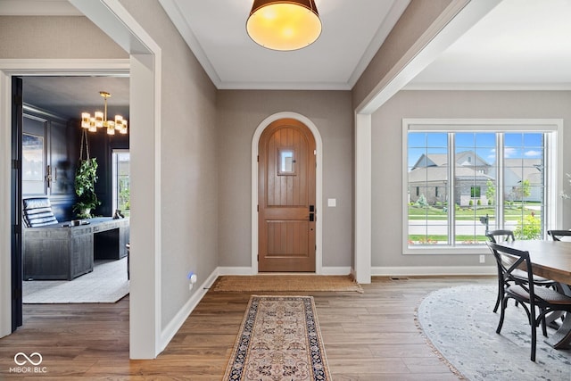 foyer featuring baseboards, arched walkways, wood finished floors, crown molding, and a chandelier