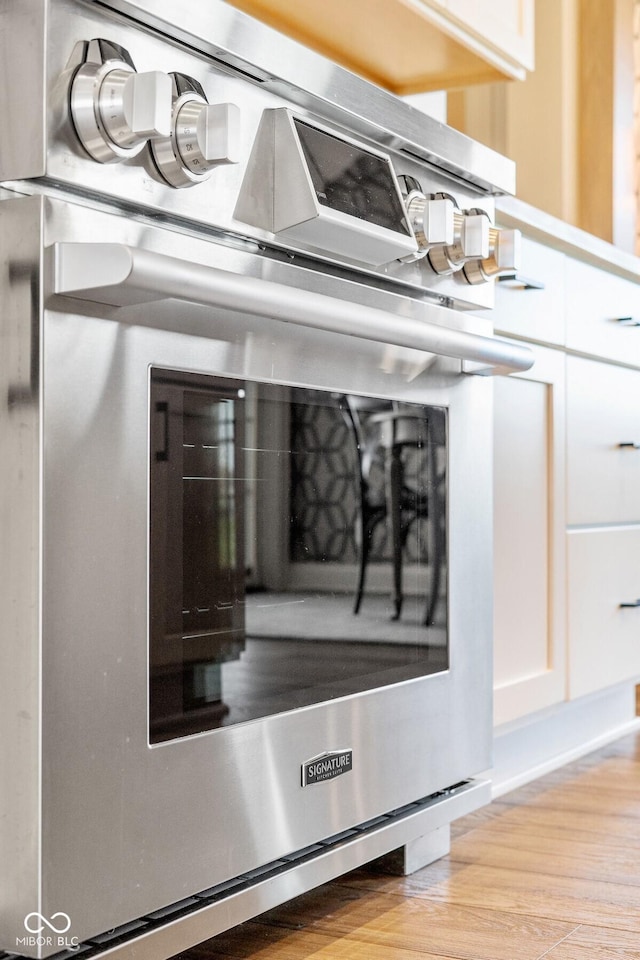 room details featuring stainless steel stove, light wood finished floors, wall oven, and white cabinetry