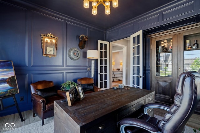 home office featuring french doors, crown molding, a decorative wall, an inviting chandelier, and light wood-style floors