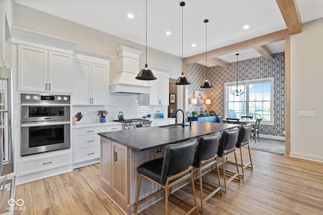 kitchen featuring custom range hood, a sink, a kitchen island with sink, and white cabinets