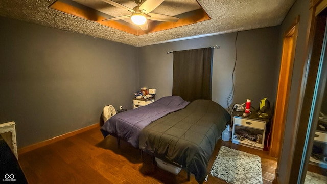 bedroom featuring a textured ceiling, ceiling fan, hardwood / wood-style flooring, and a tray ceiling