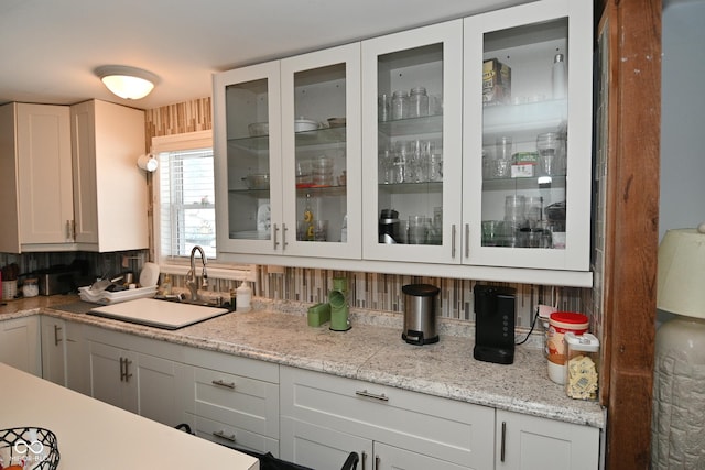 kitchen with decorative backsplash, light stone countertops, sink, and white cabinetry