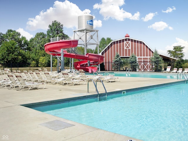 pool featuring a water slide, a patio area, fence, and a barn