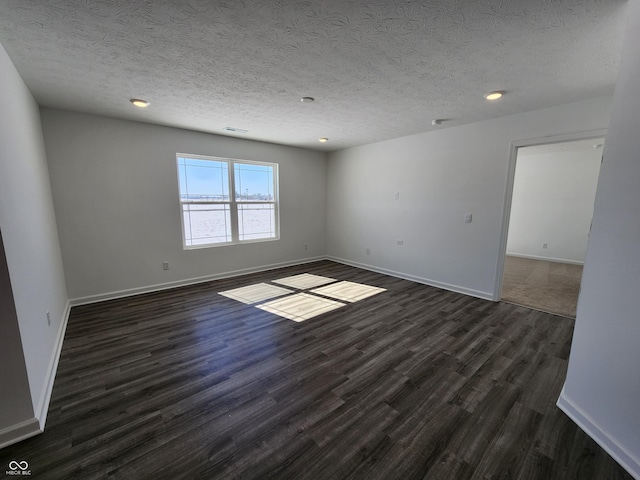 empty room featuring a textured ceiling, baseboards, and dark wood-type flooring