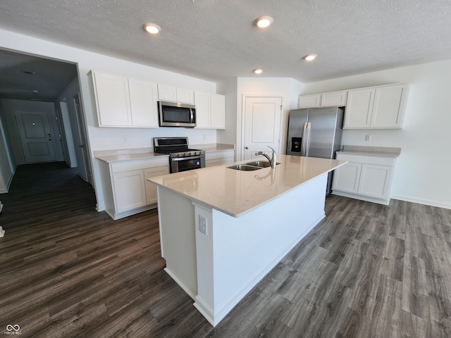 kitchen with a kitchen island with sink, dark wood-type flooring, a sink, white cabinets, and appliances with stainless steel finishes